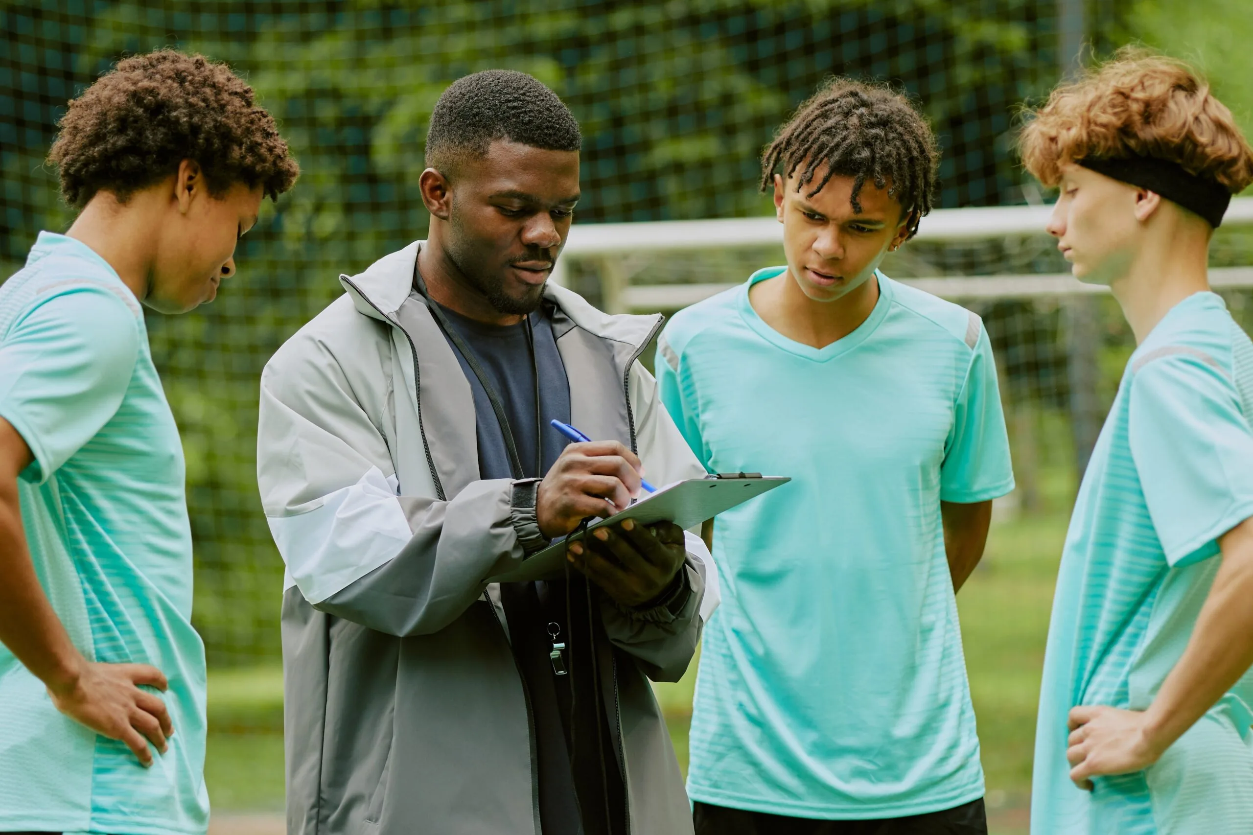 Soccer coach reviewing a clipboard with three teenage players on a field.