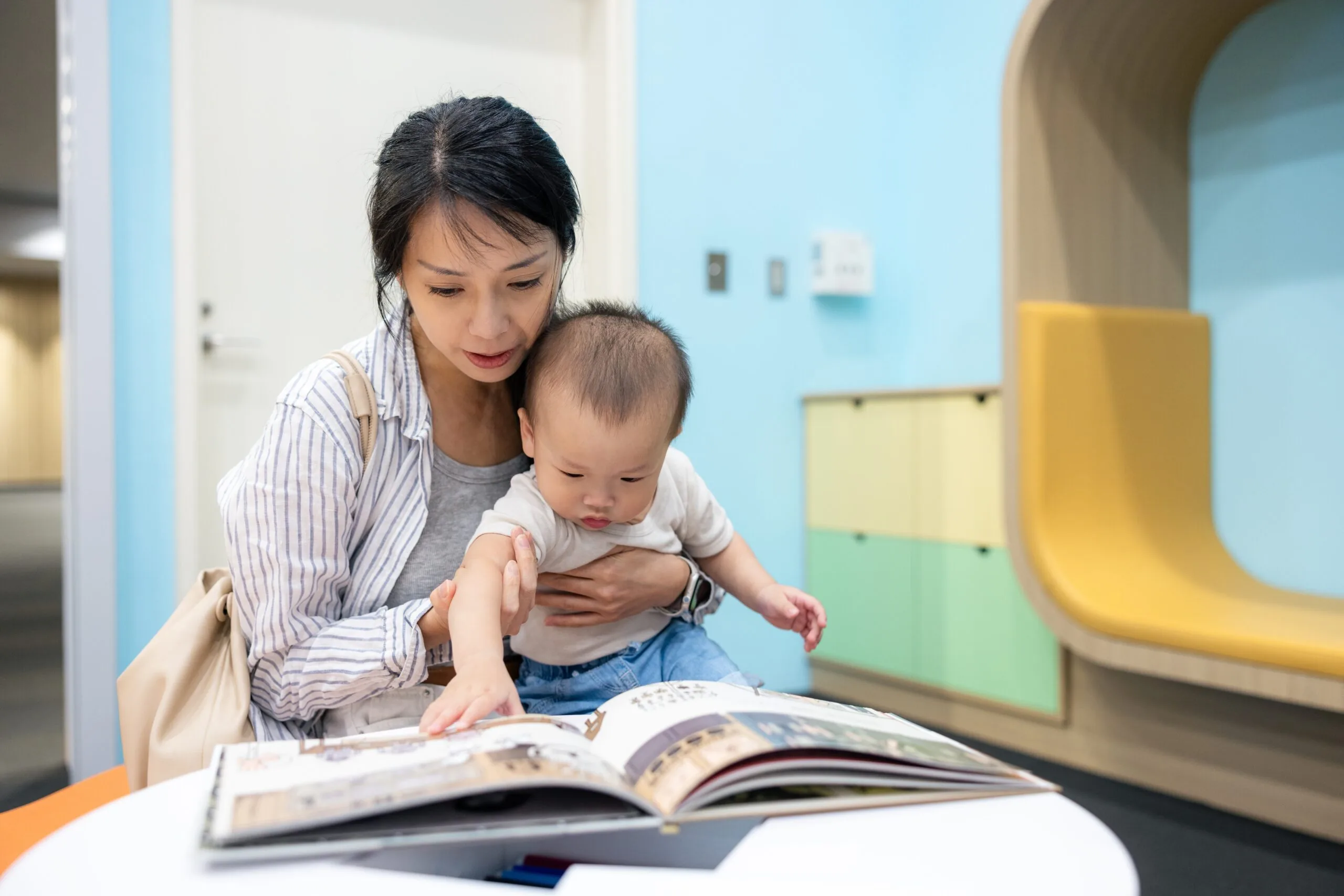 An adult and young child reading a picture book together in a library.