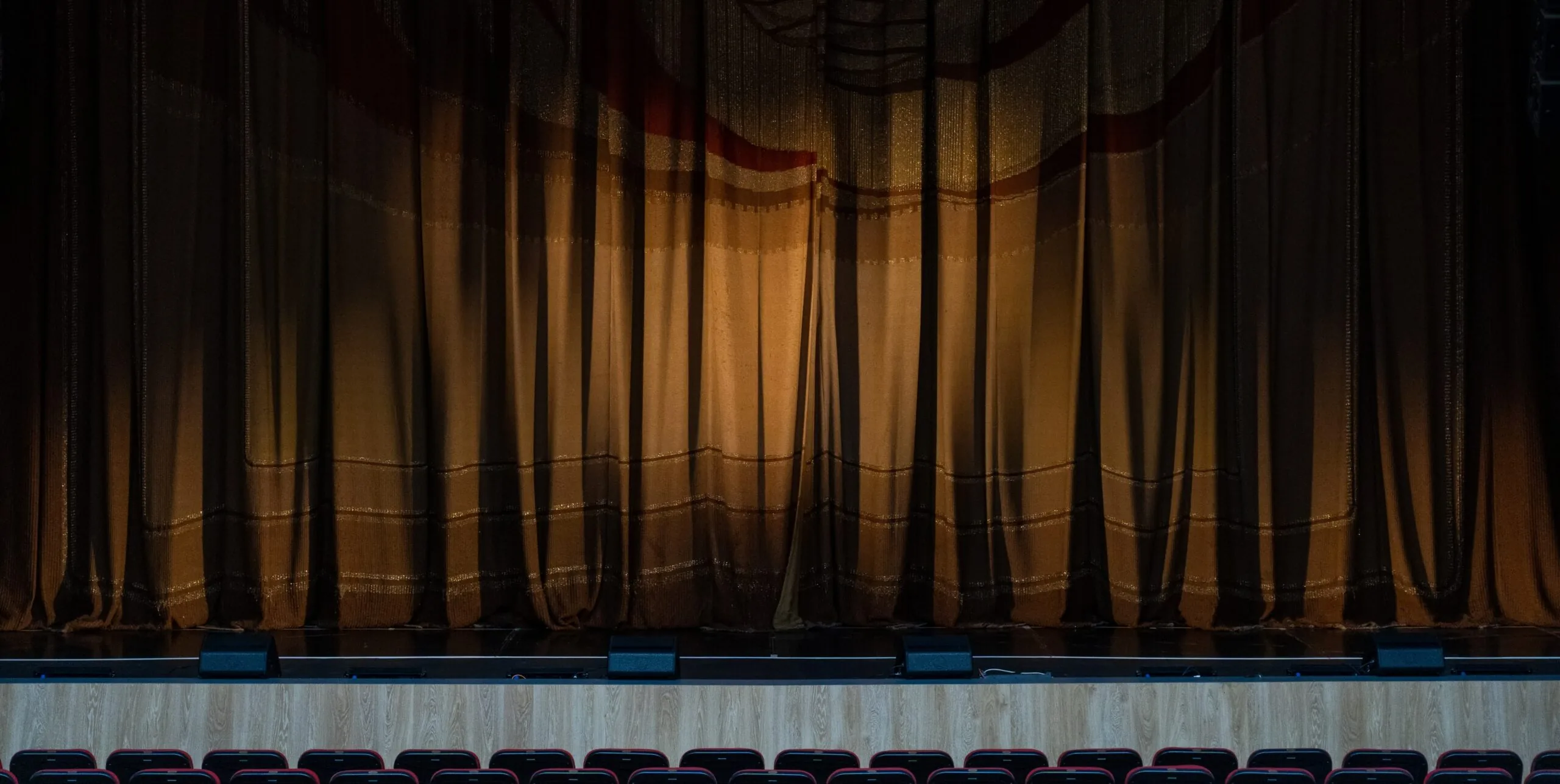 Curtained theater stage facing rows of empty seats Illustrative photograph.