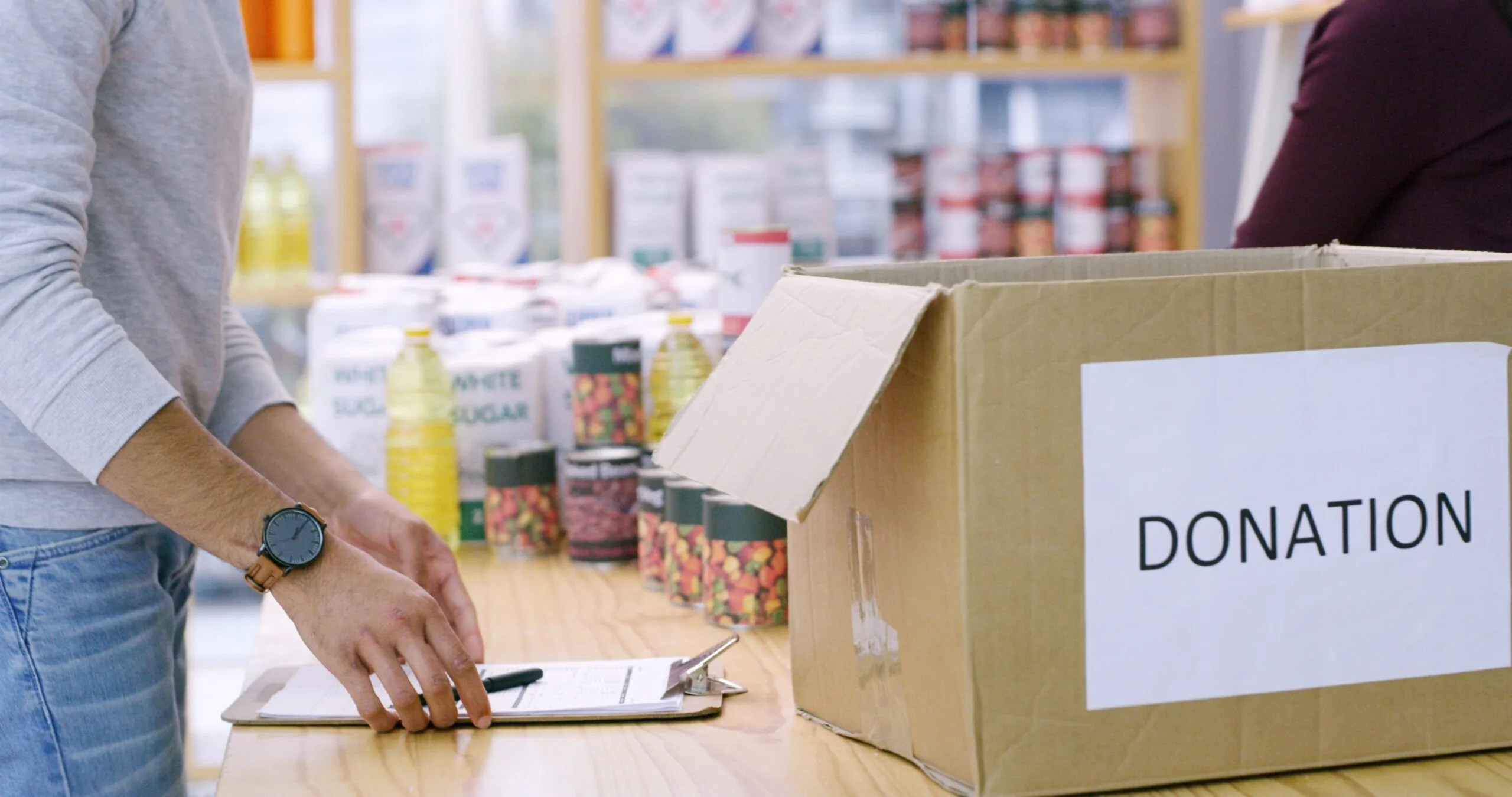 Volunteer checking a clipboard beside a food donation box.