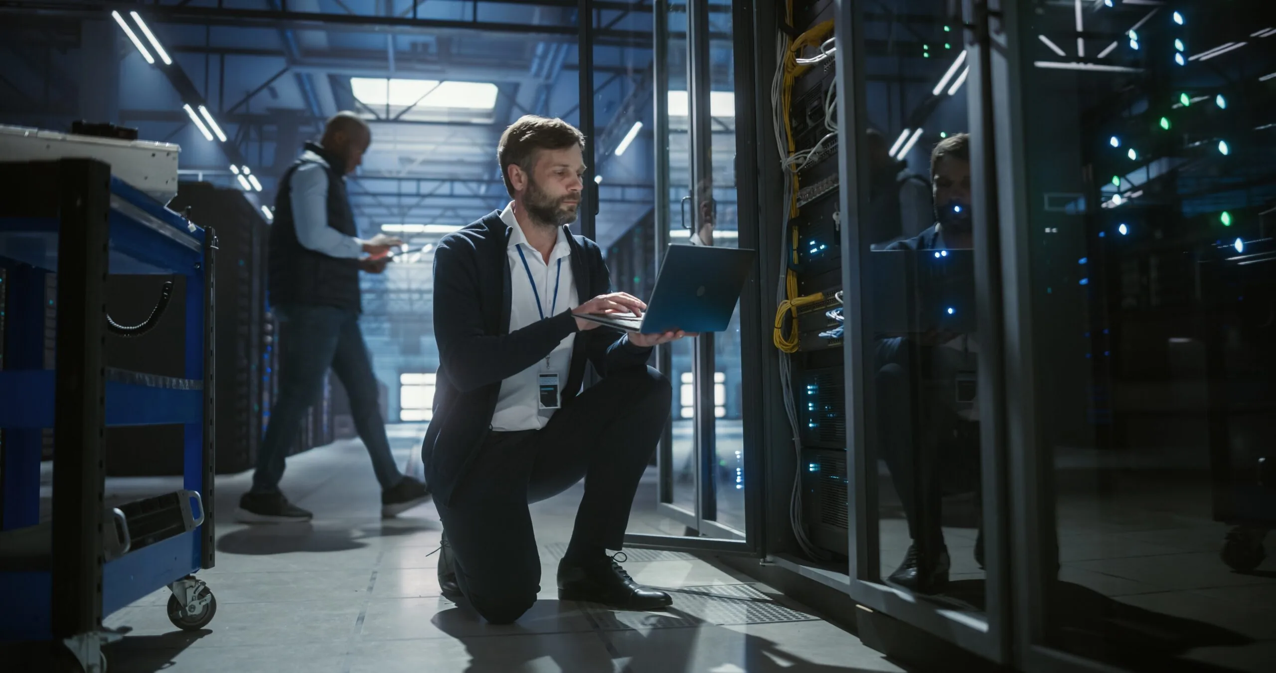 Technician using a laptop beside data-center server racks.