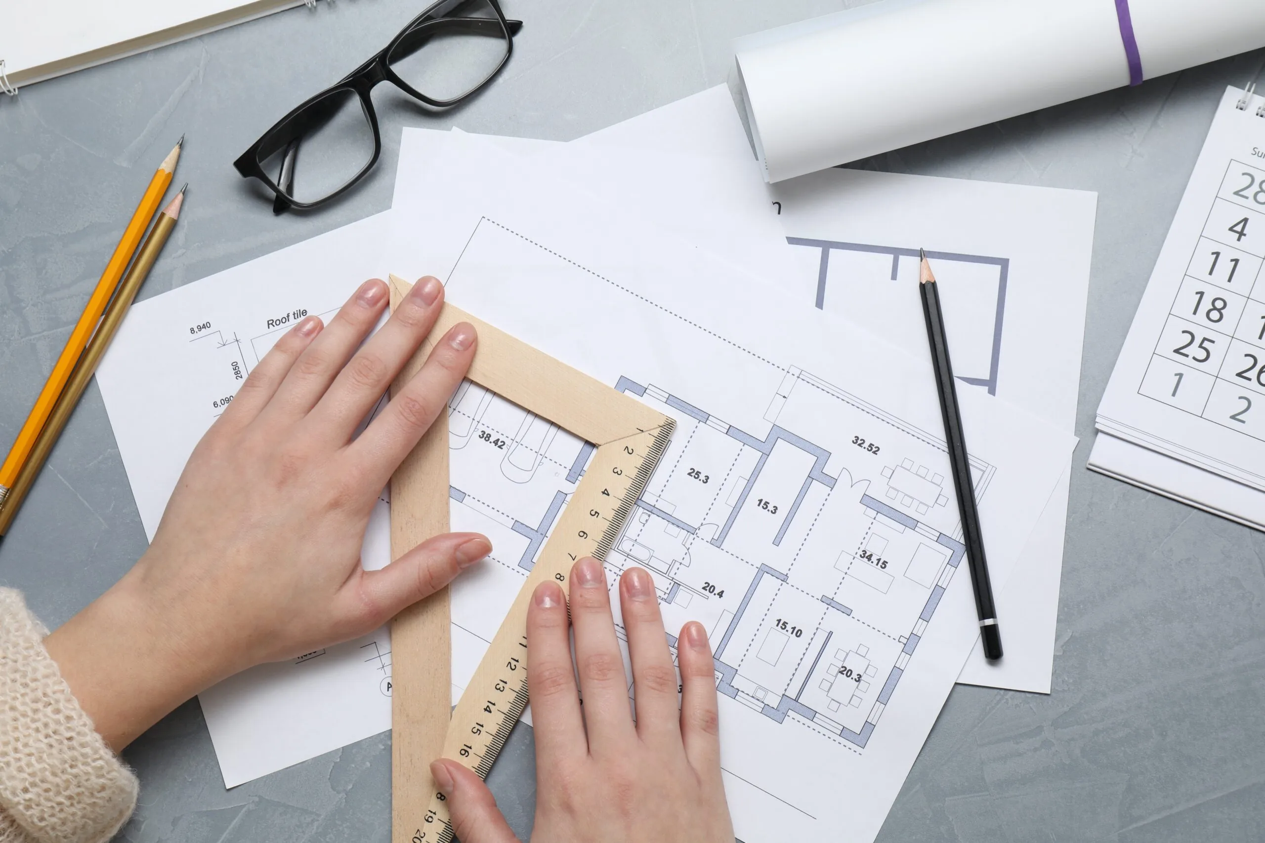 Hands measuring a house floor plan with a set-square ruler.