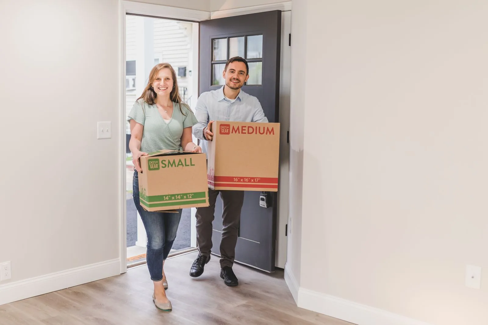 Couple carrying moving boxes through the front door of a home