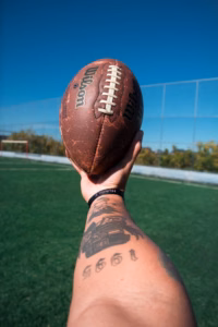 A hand holding an American football on a field; illustrative photograph
