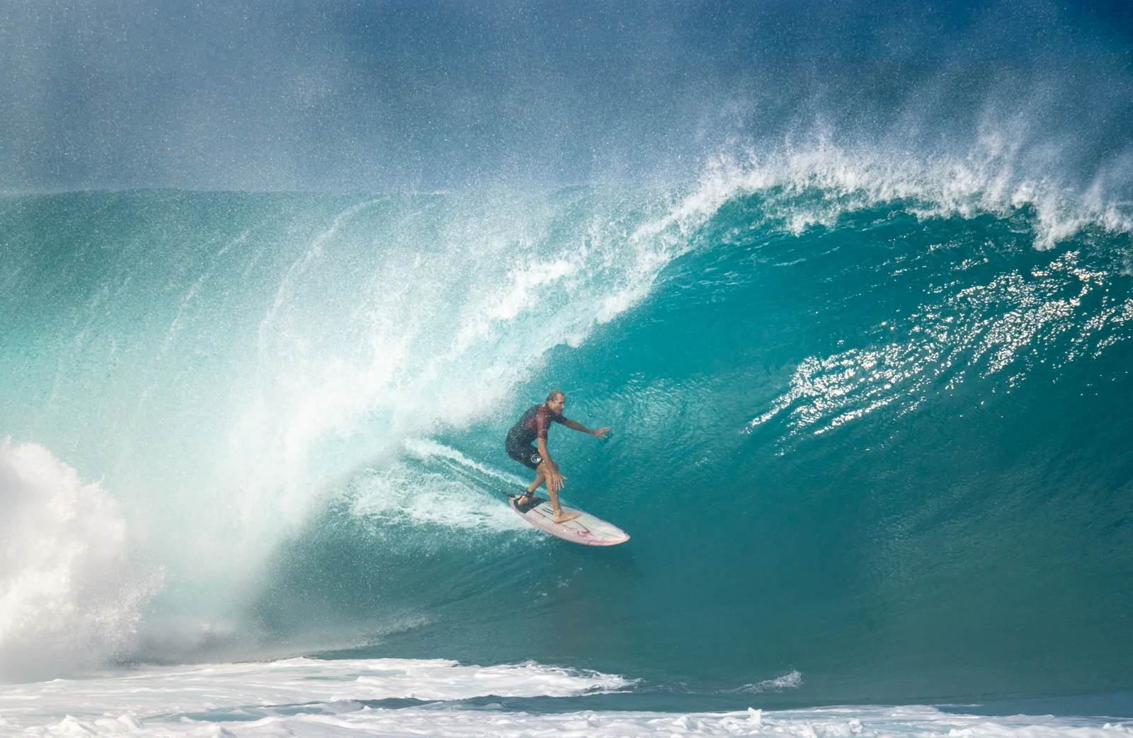 A surfer riding across a breaking blue ocean wave.